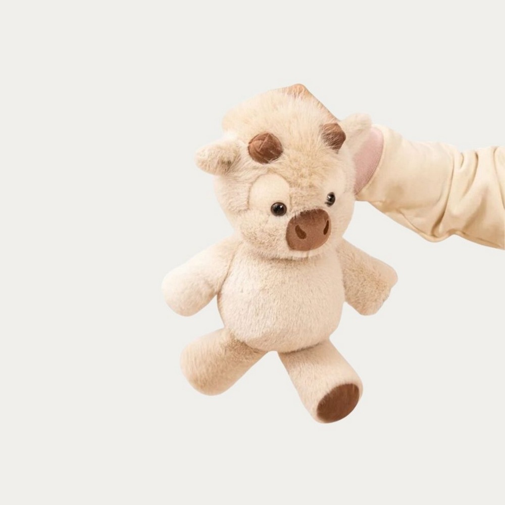 Une main tient la Peluche vache interactive aux pattes mobiles, un petit doudou vache tout doux avec des yeux ronds, sur un fond blanc simple.