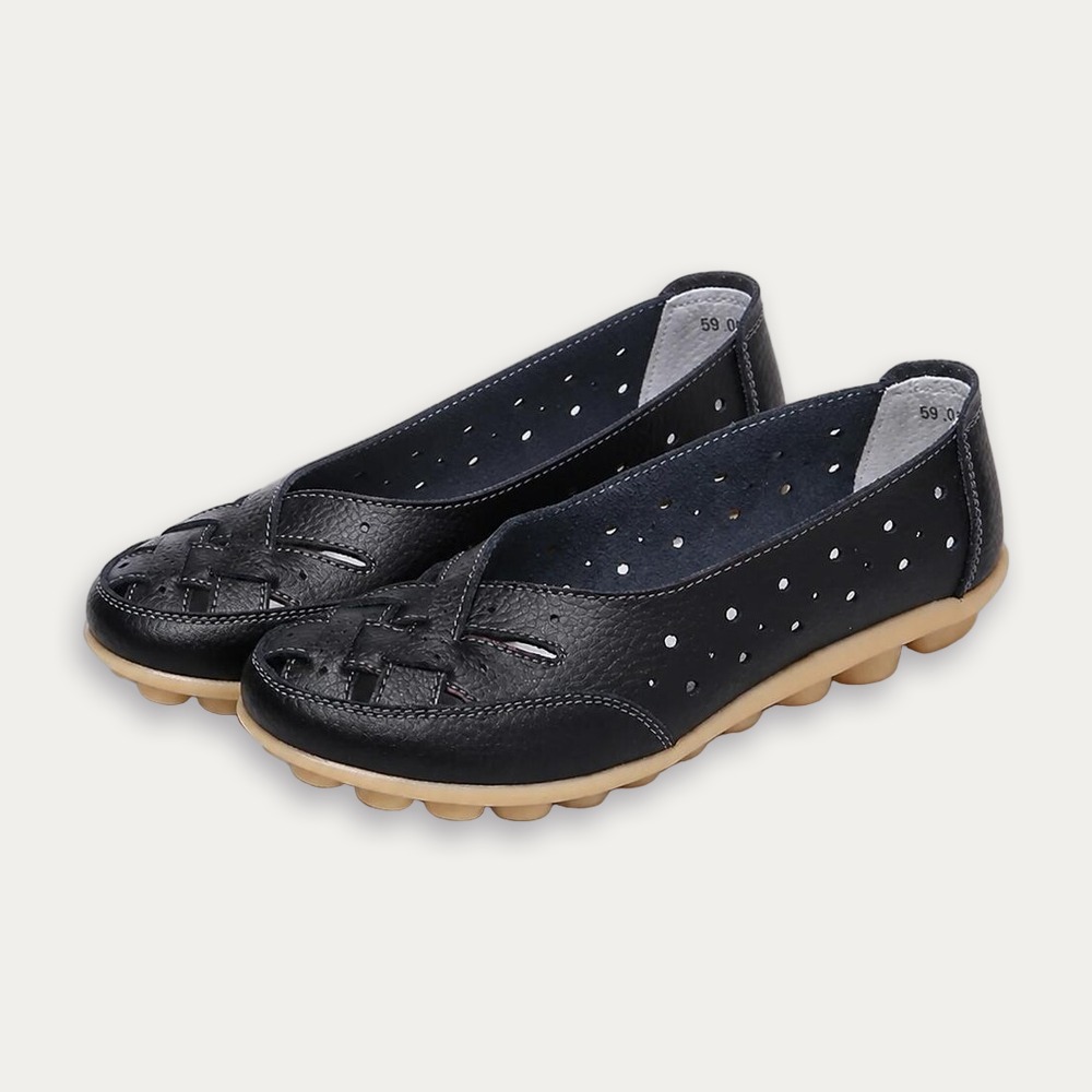 Une paire de ballerines confortables ajourées en cuir noires avec petite semelle beige, posées sur fond clair.