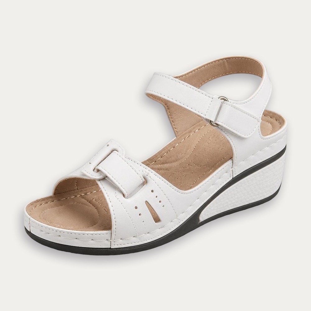 Une paire de sandales orthopédiques tendances à talon compensé blanches, avec brides réglables et semelle épaisse, posée sur fond clair.